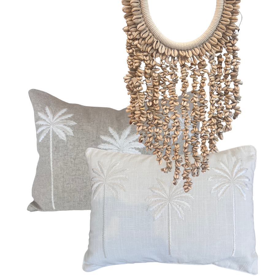 Two linen cushion covers with embroidered palm trees and a cowrie shell hanging.