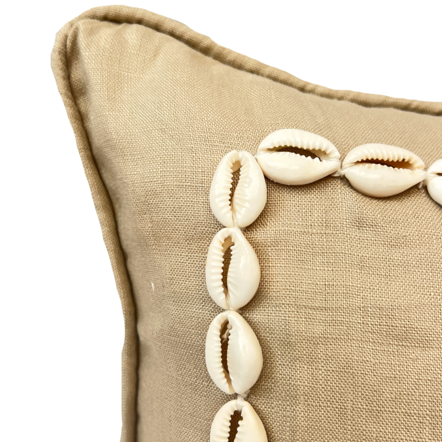 Beige cushion with shell decorations on a beige background.