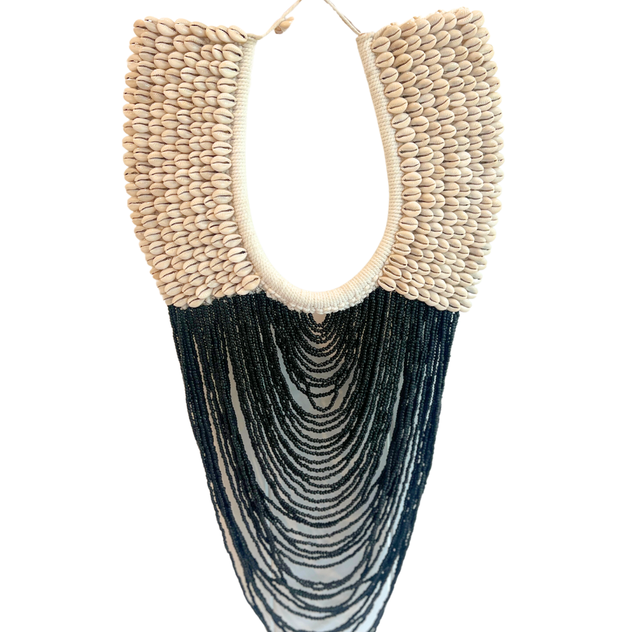 A large cowrie shell wall hanging with black beading, designed to be displayed on a wall as a necklace-shaped decoration.