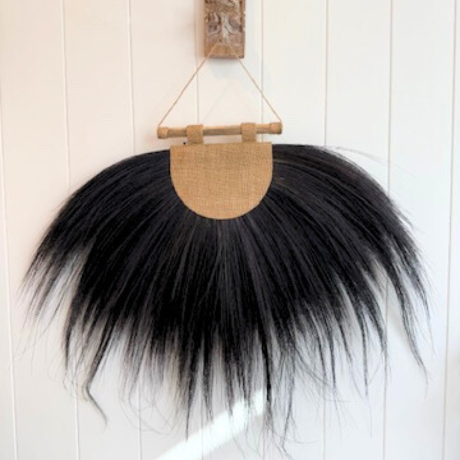 Black feathered wall hanging with a wooden base on a white wooden panel background.