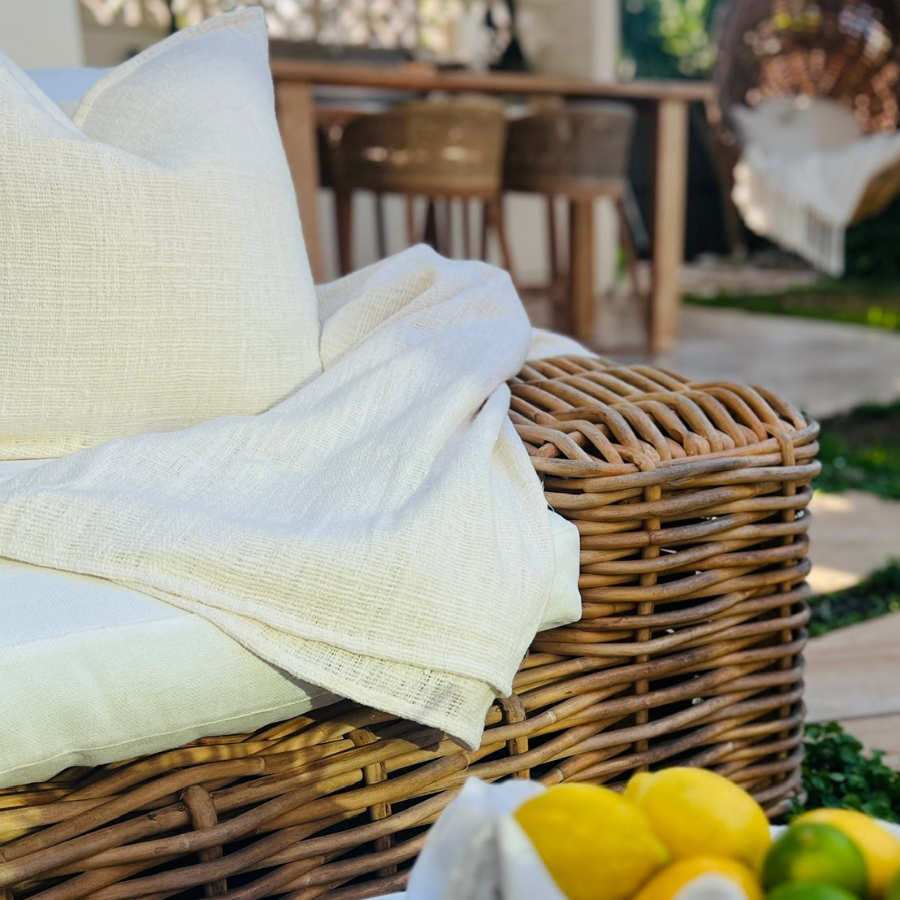 White cushion and blanket on a rattan chair with fruit decor.