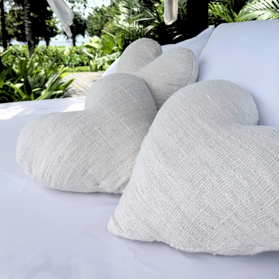 Heart-shaped cushions on a white surface with a tropical outdoor setting in the background.