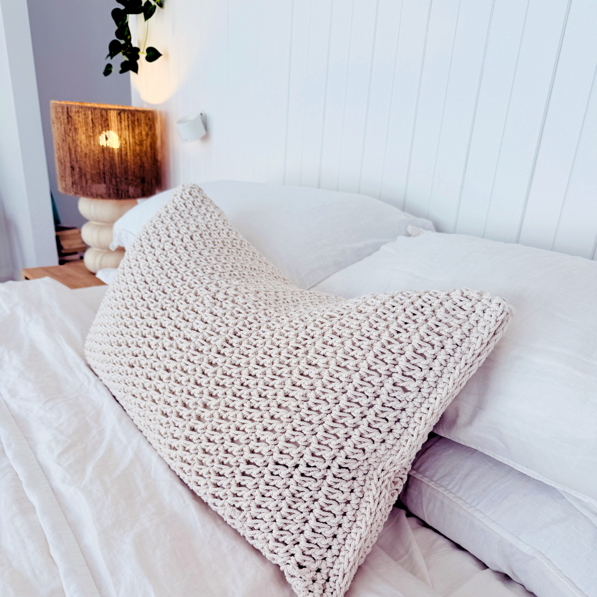 Cozy bedroom with a textured cushion on a bed, nightstand with lamp, and white walls.