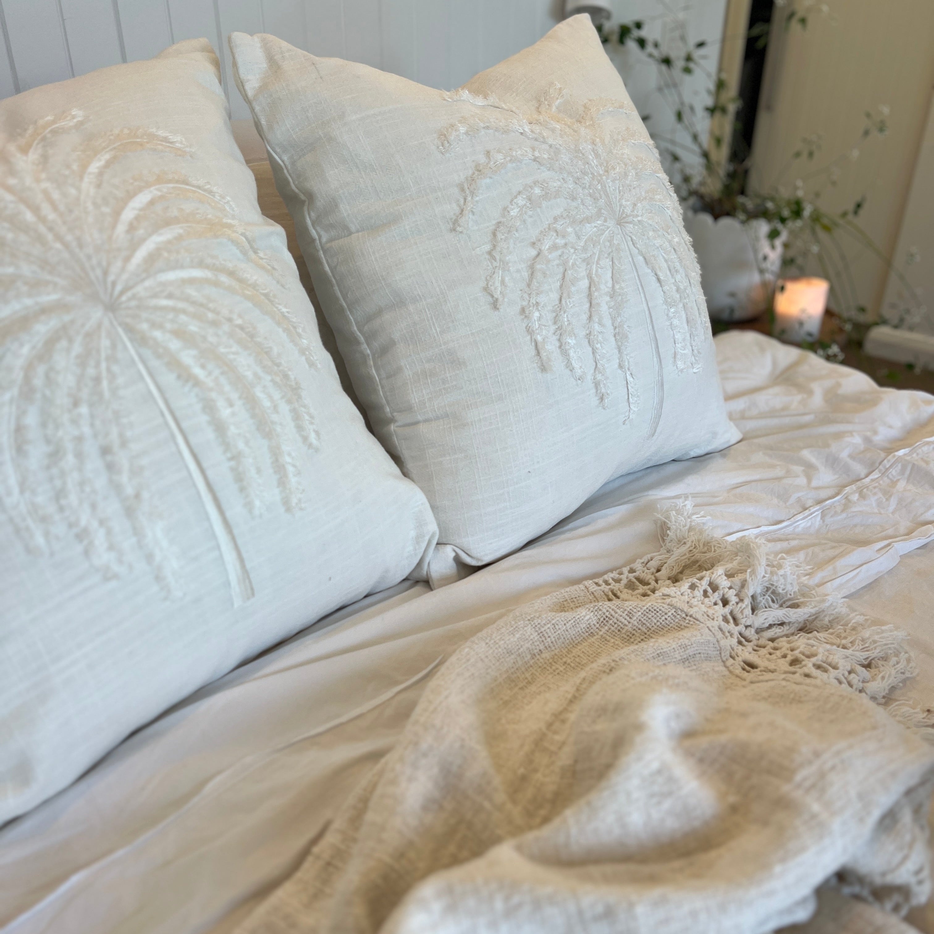 White cushion with palm tree design on a bed.