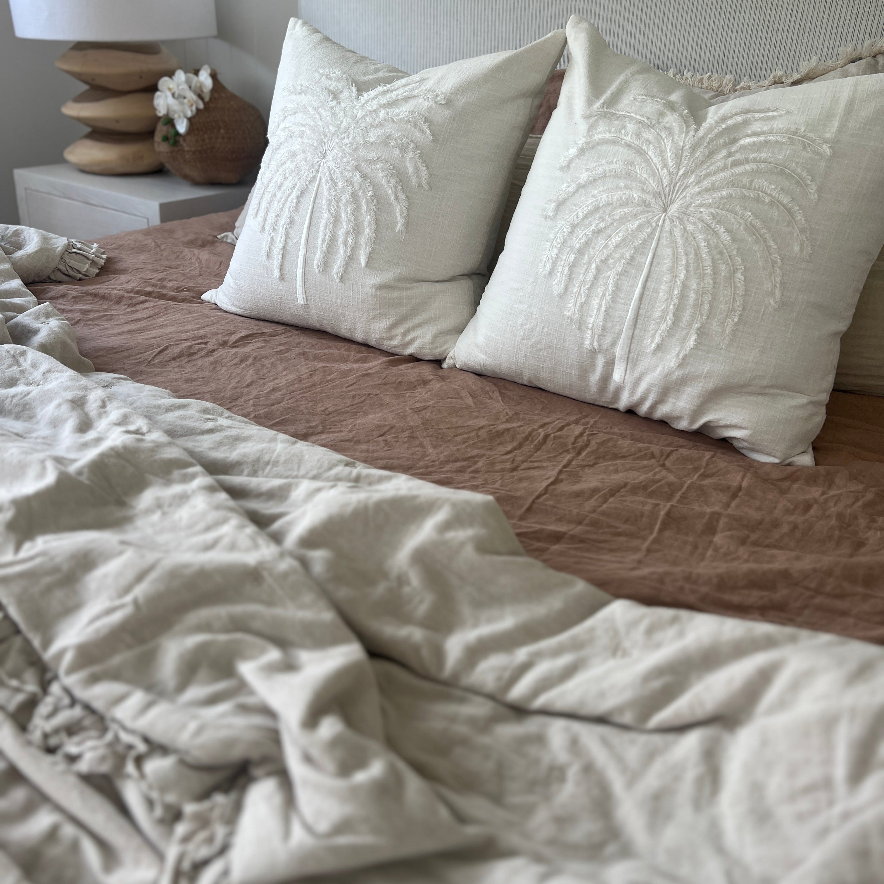 White cushion with palm tree decor on a bed with blanket. 