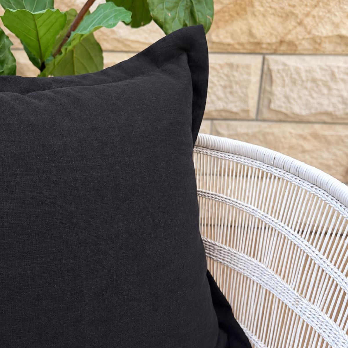 Black linen cushion close-up styled on a white woven chair.