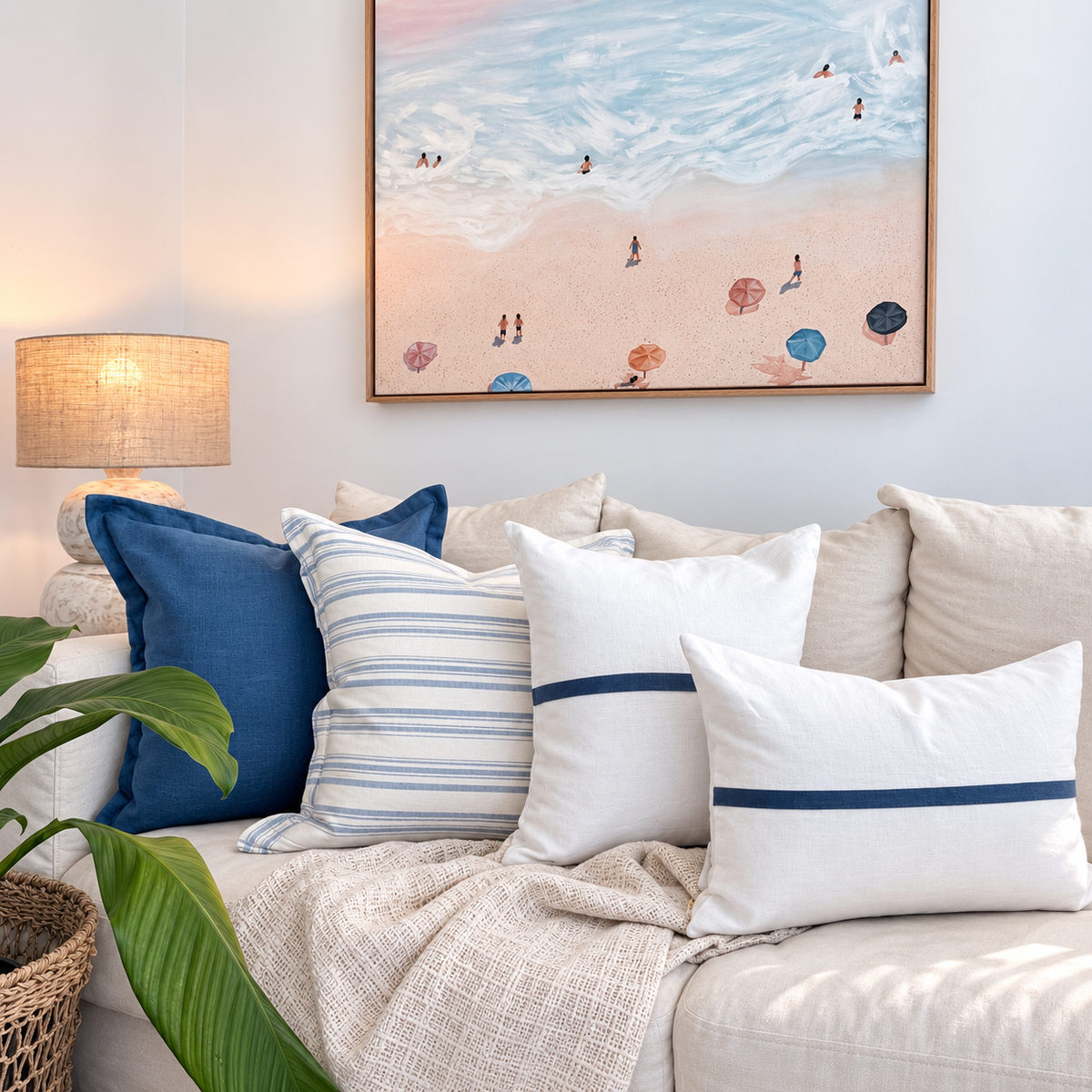 Blue and white linen cushion collection styled on a white sofa beneath beach artwork.