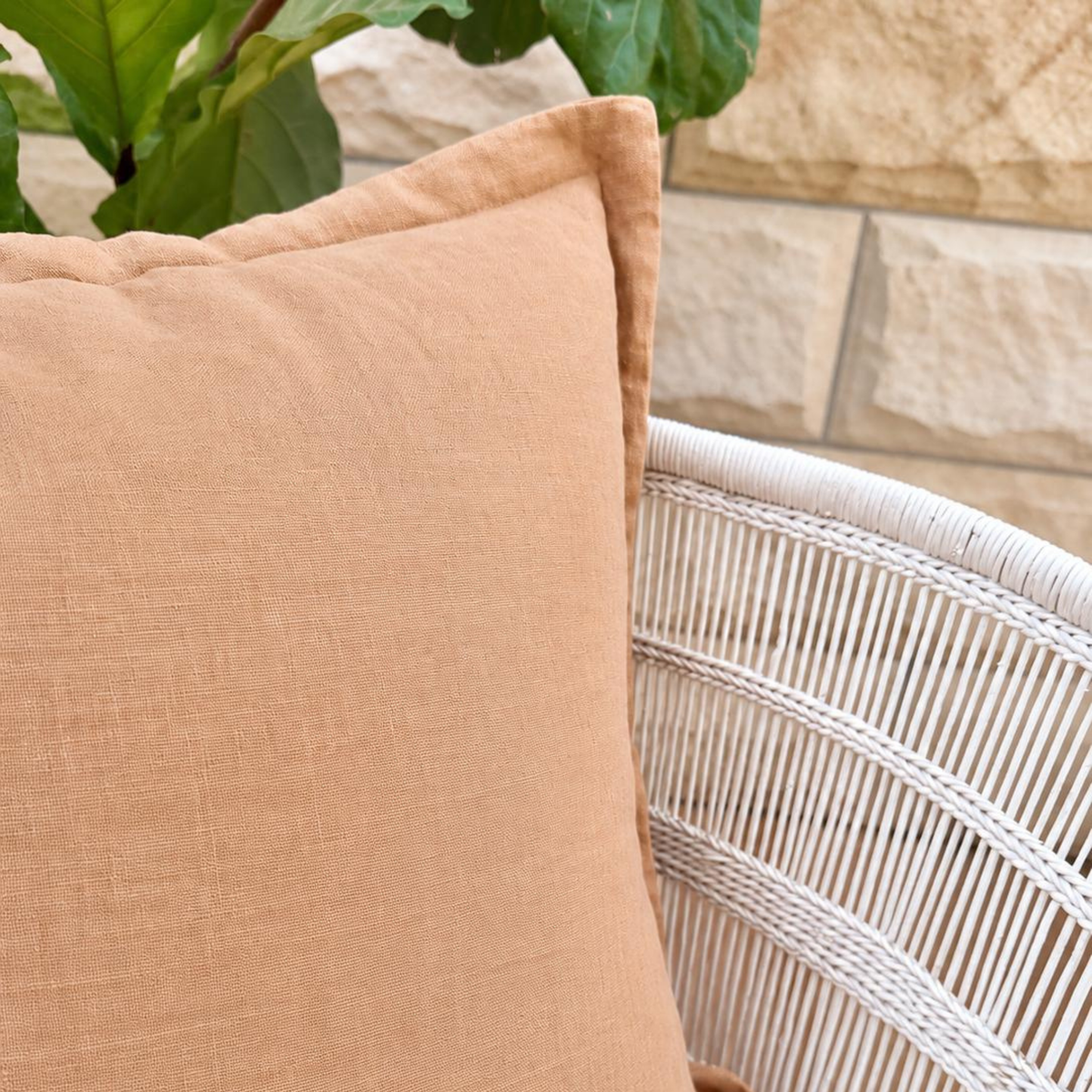 Cinnamon linen cushion close-up styled on a white woven chair.