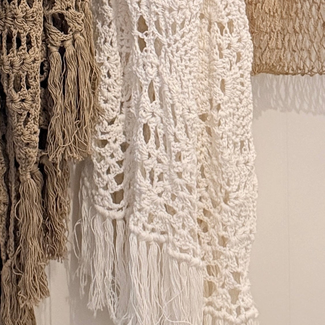 Close-up of crocheted throw blankets with fringe detail hanging on display.