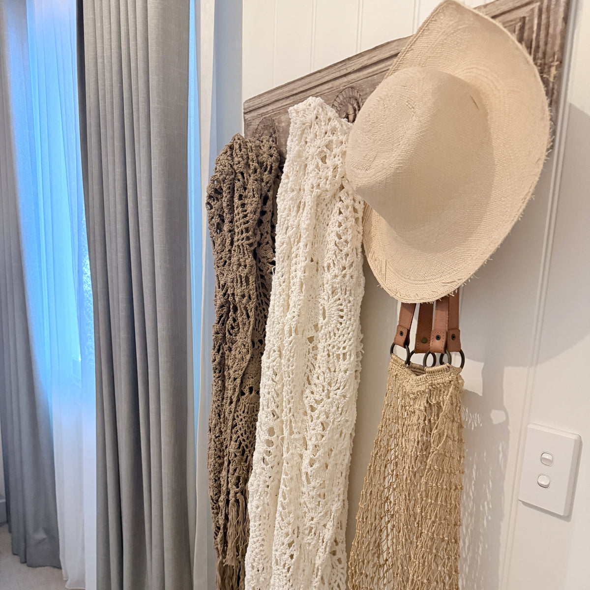 Crocheted throws, straw sun hat, and woven bag hanging on a rustic wooden wall rack.
