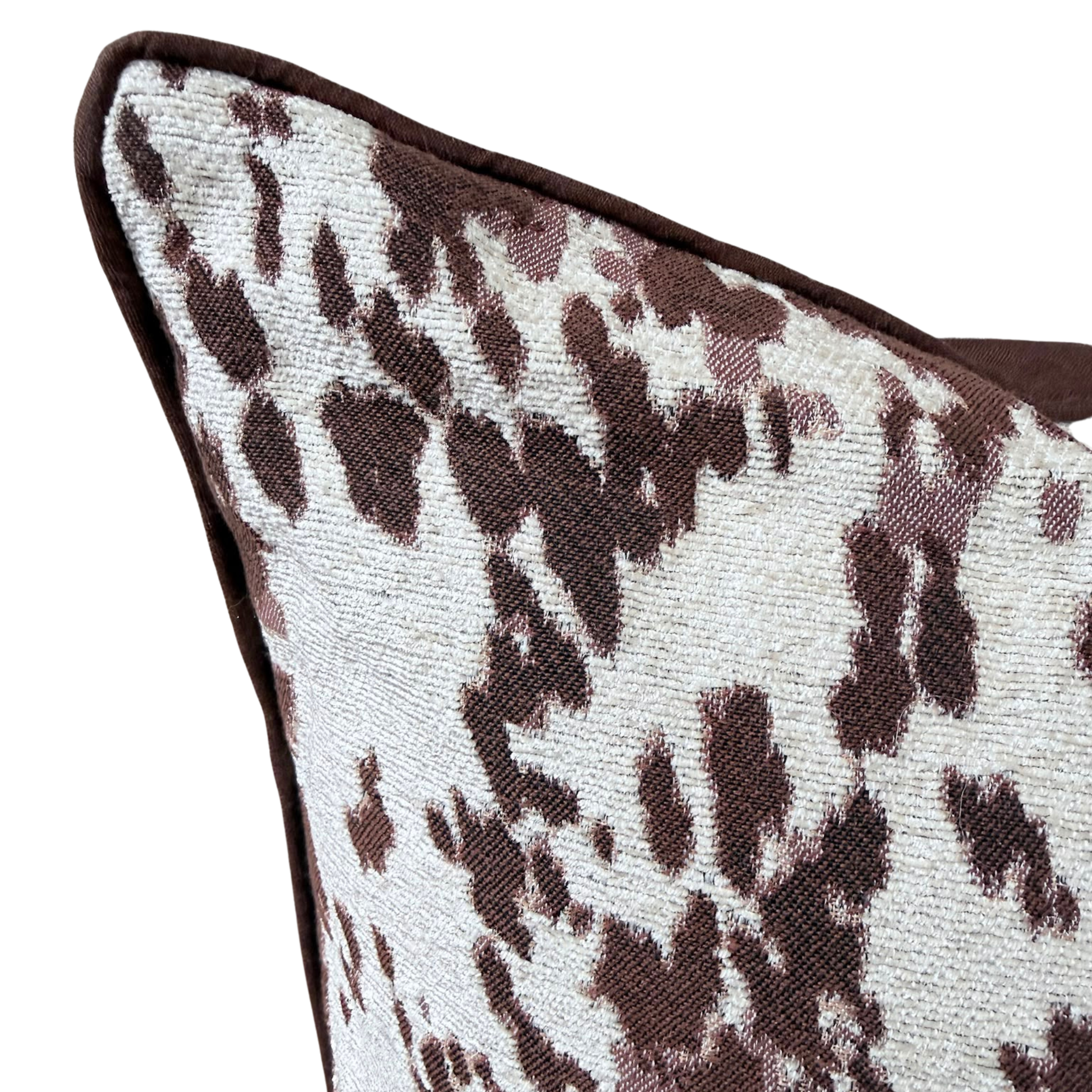 Close-up of a square throw cushion featuring a brown and off-white leopard print pattern with a dark brown piped edge.