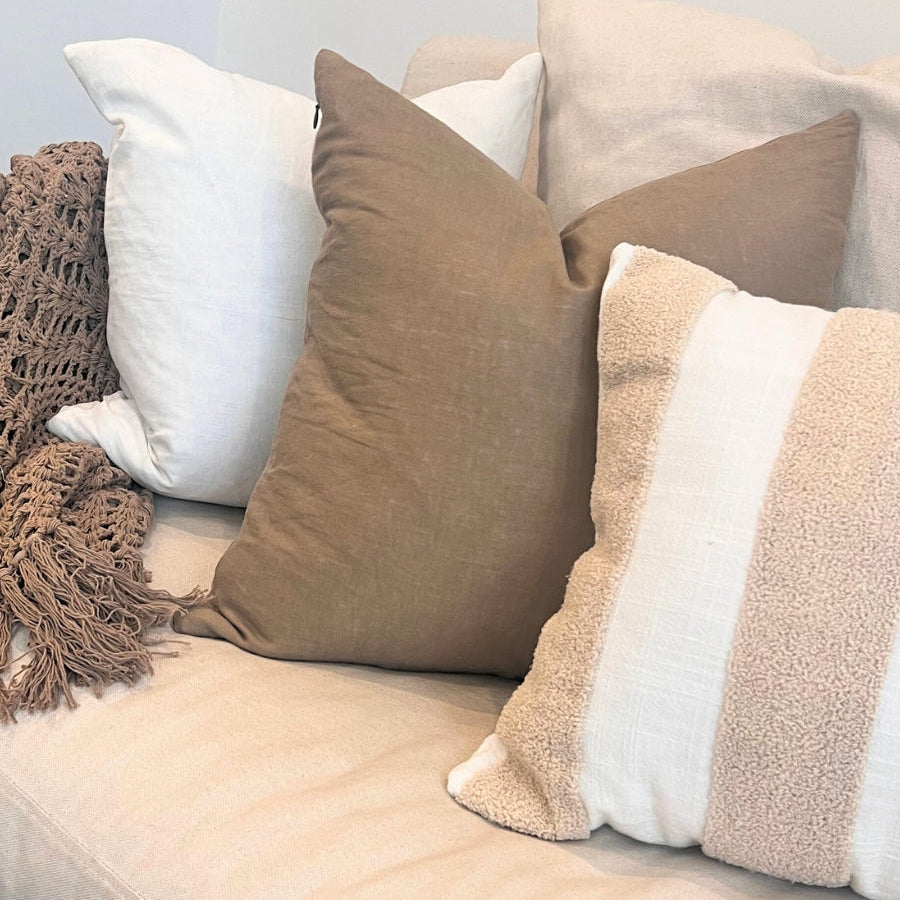 Solid brown and striped brown cushions on a sofa with blanket.
