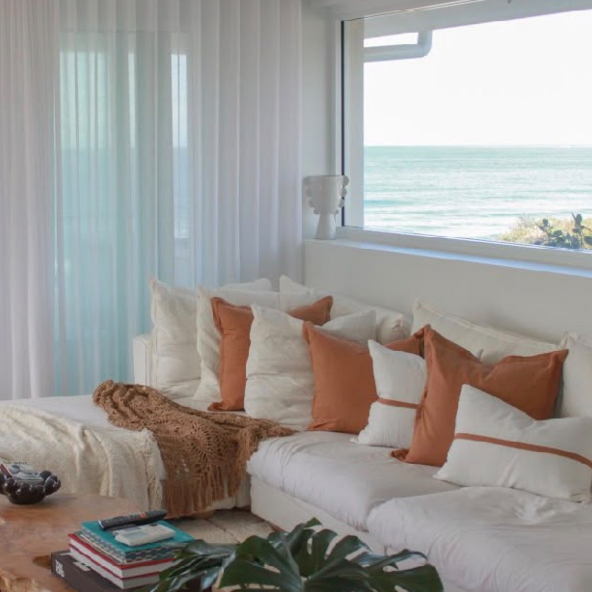 Cinnamon and white cushion arrangement on a sectional couch in a coastal living room with sea views.