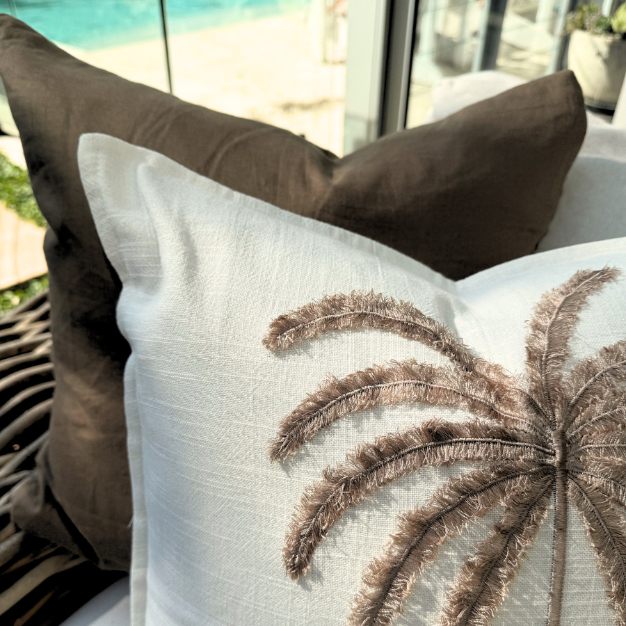 Decorative cushion with palm tree design on a couch outdoors.