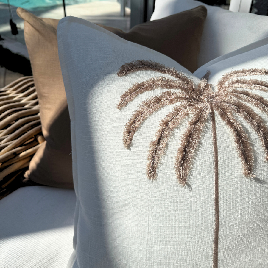 Decorative cushion with palm tree design on a couch near a pool.