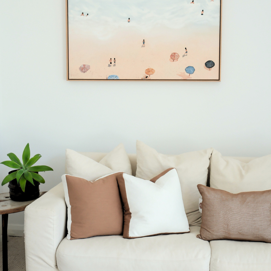 Framed artwork above a sofa with decorative cushion in a living room setting.
