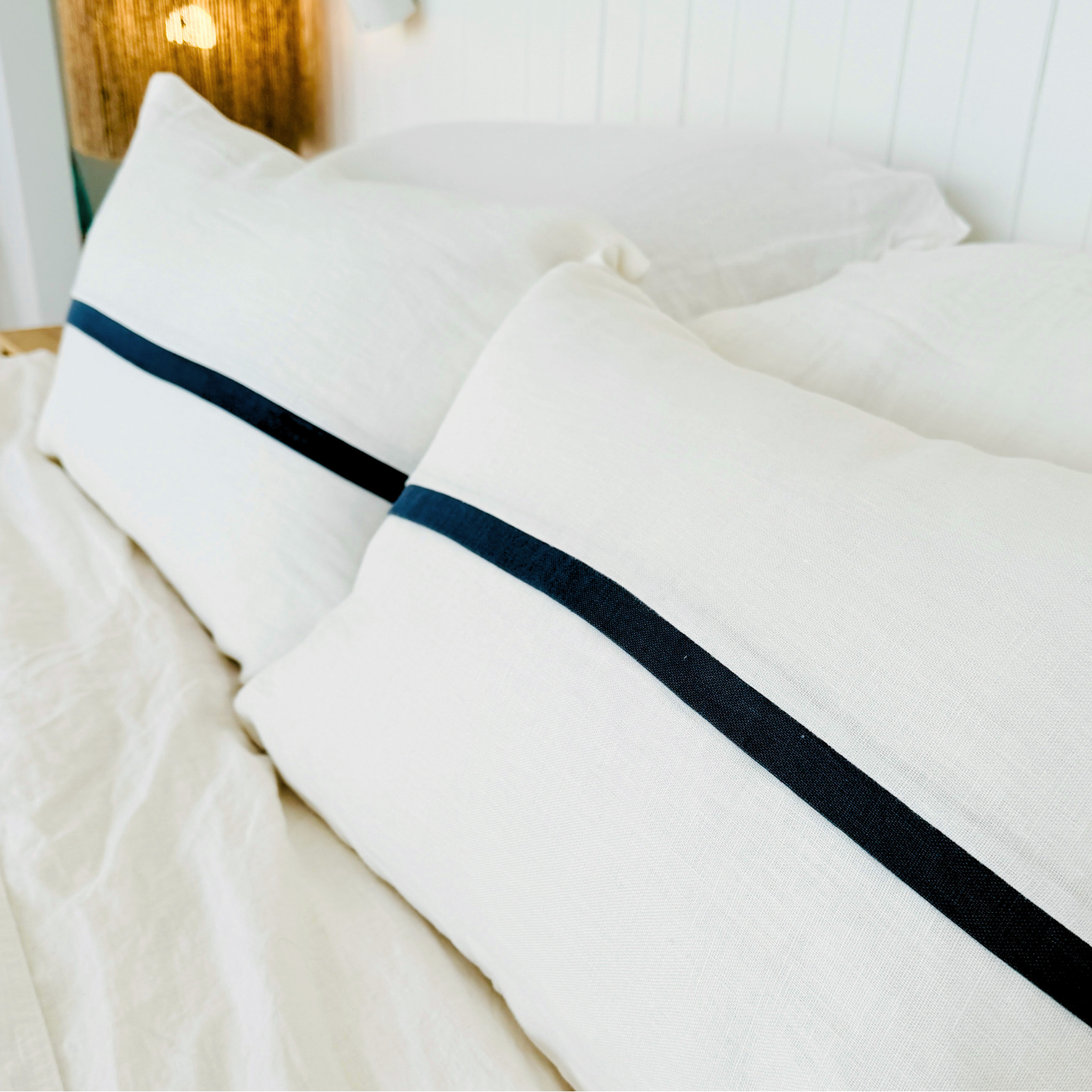 White cushion with navy blue stripes on a bed in a bedroom setting.