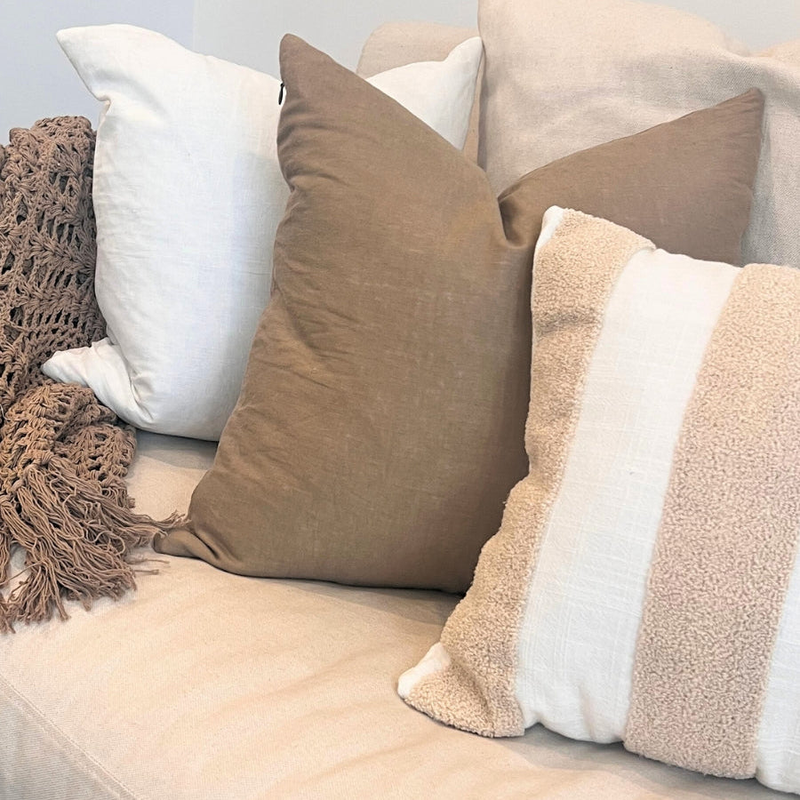Brown and white cushions on a sofa with blanket. 
