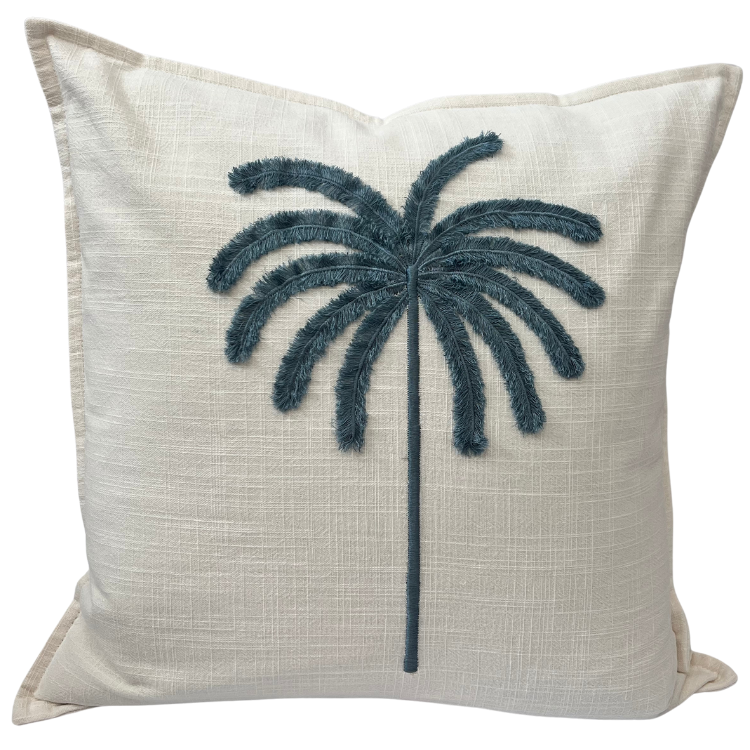 A square-shaped cushion cover with a tufted embroidered palm design in blue on an ivory background.